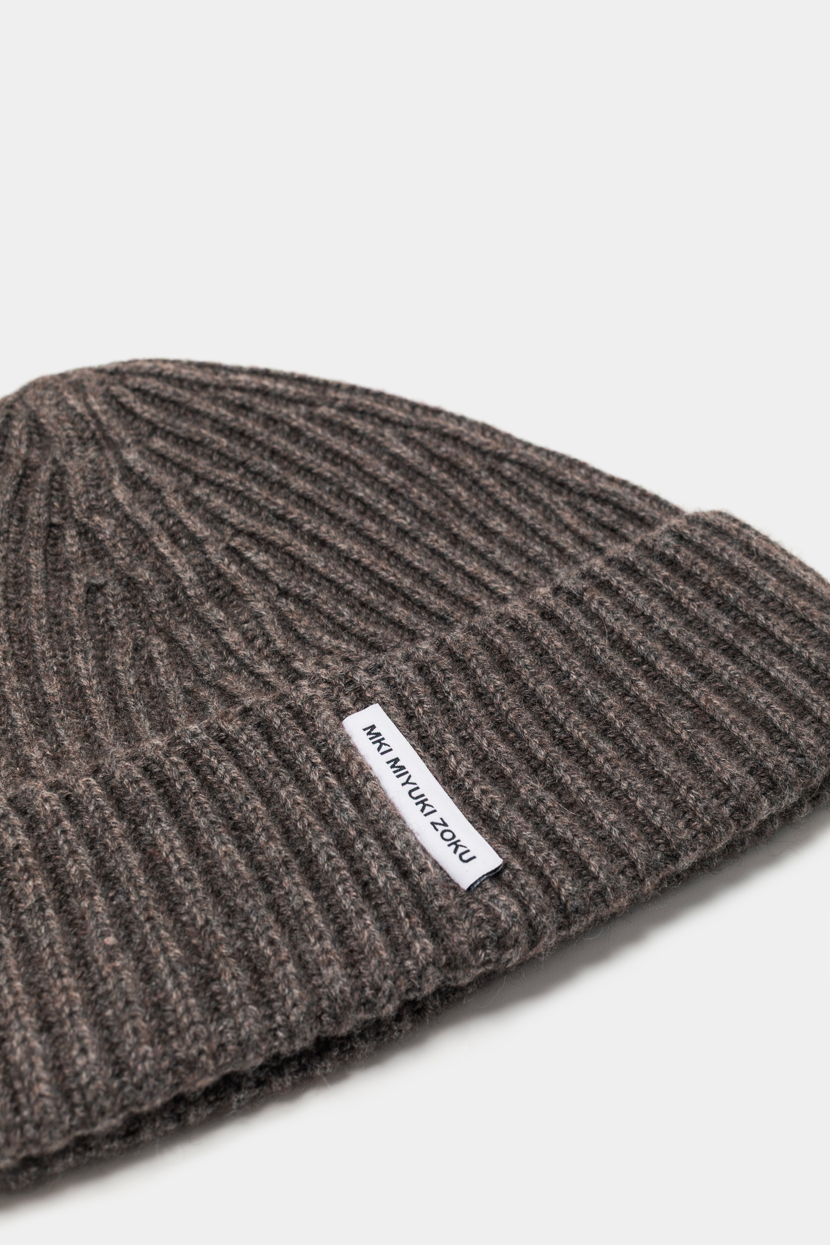 Close-up of the woven MKI MIYUKI ZOKU tag and heavy rib knit on the Brown cashmere beanie