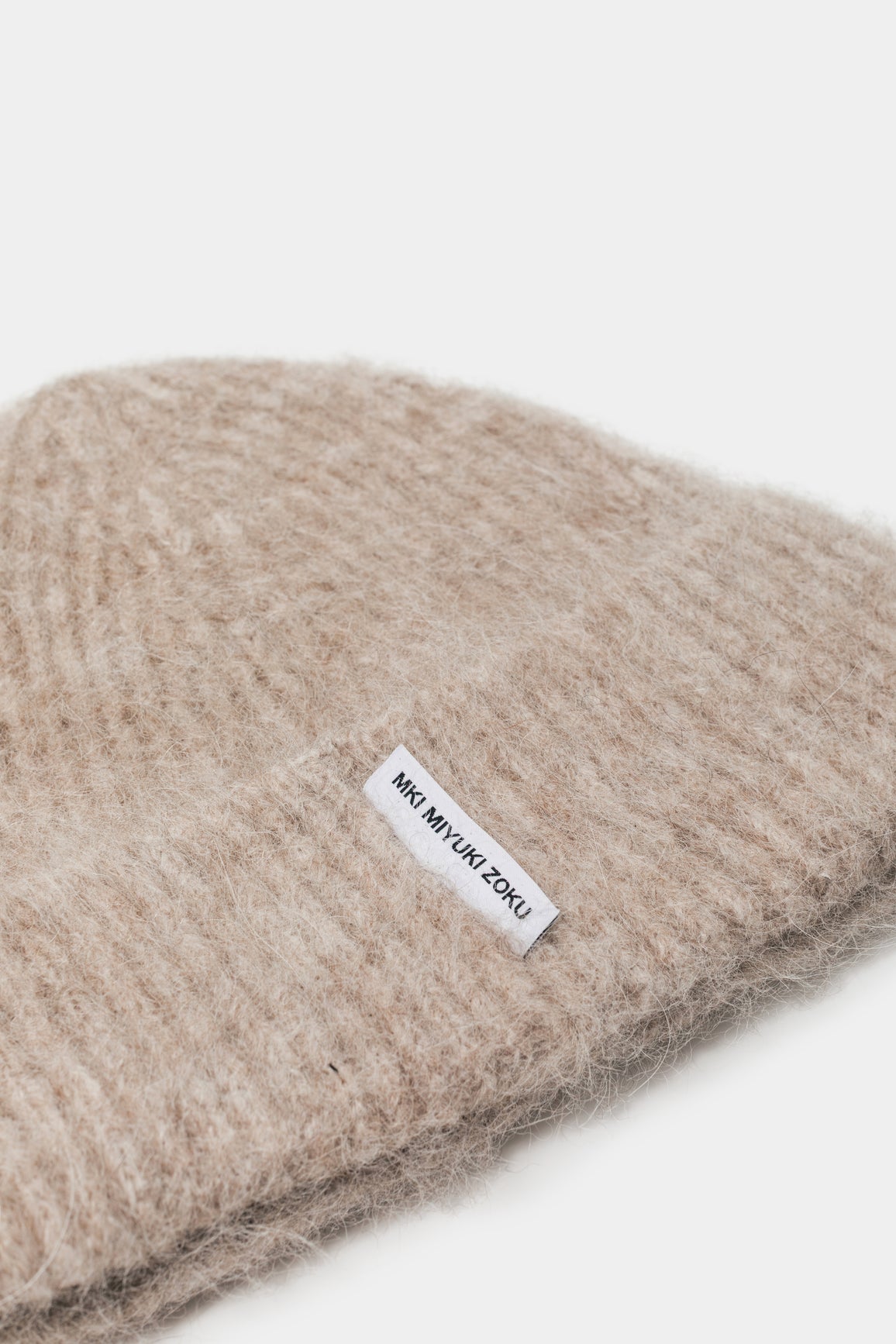 Close-up of the woven MKI MIYUKI ZOKU tag and fuzzy alpaca knit on the Oatmeal beanie