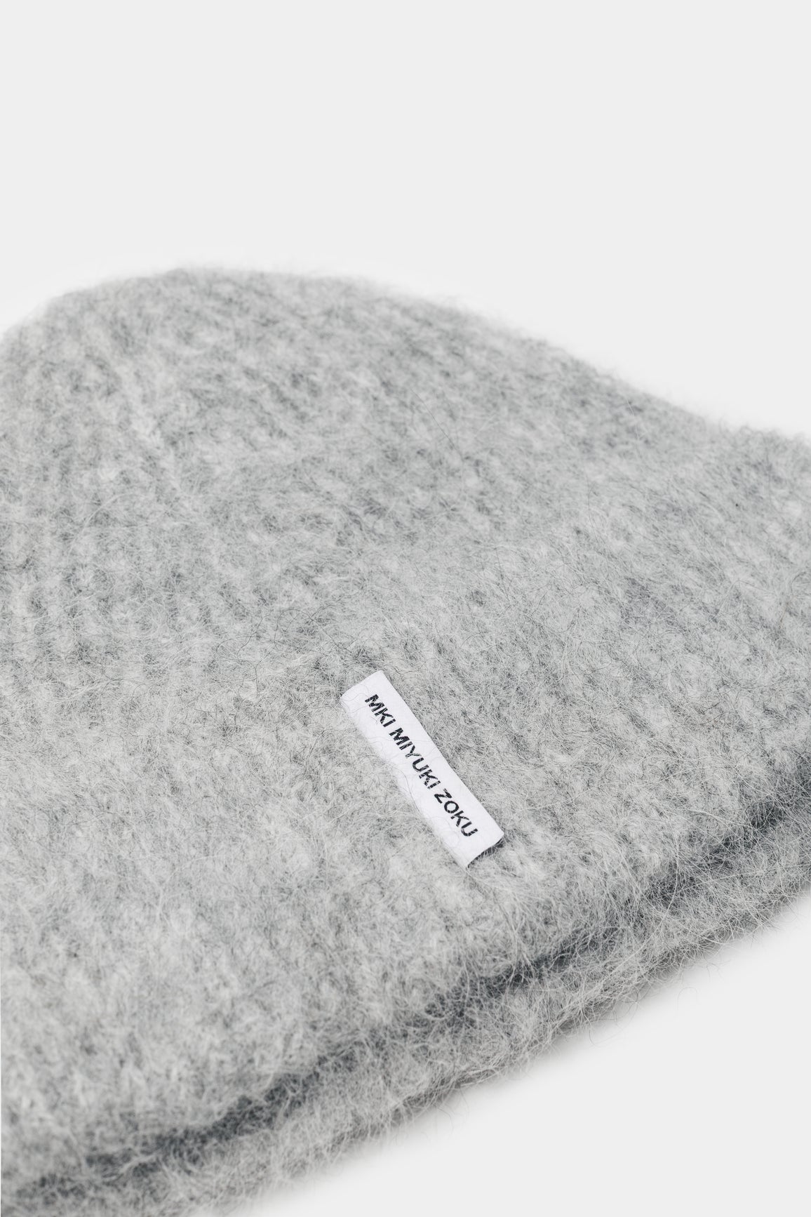 Close-up of the woven MKI MIYUKI ZOKU tag and fuzzy alpaca knit on the Light Grey beanie