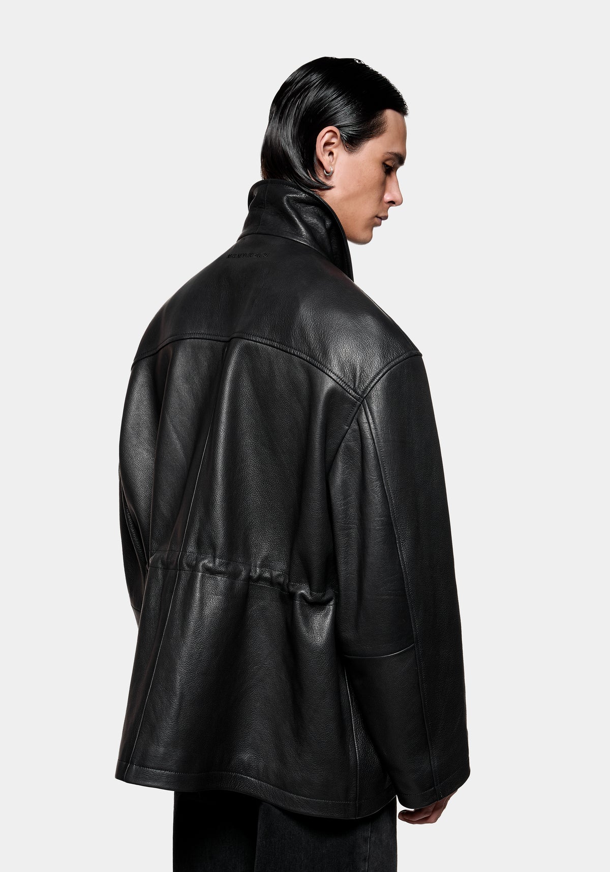 Person wearing a black leather jacket with a high collar and drawstring waist viewed from the back
