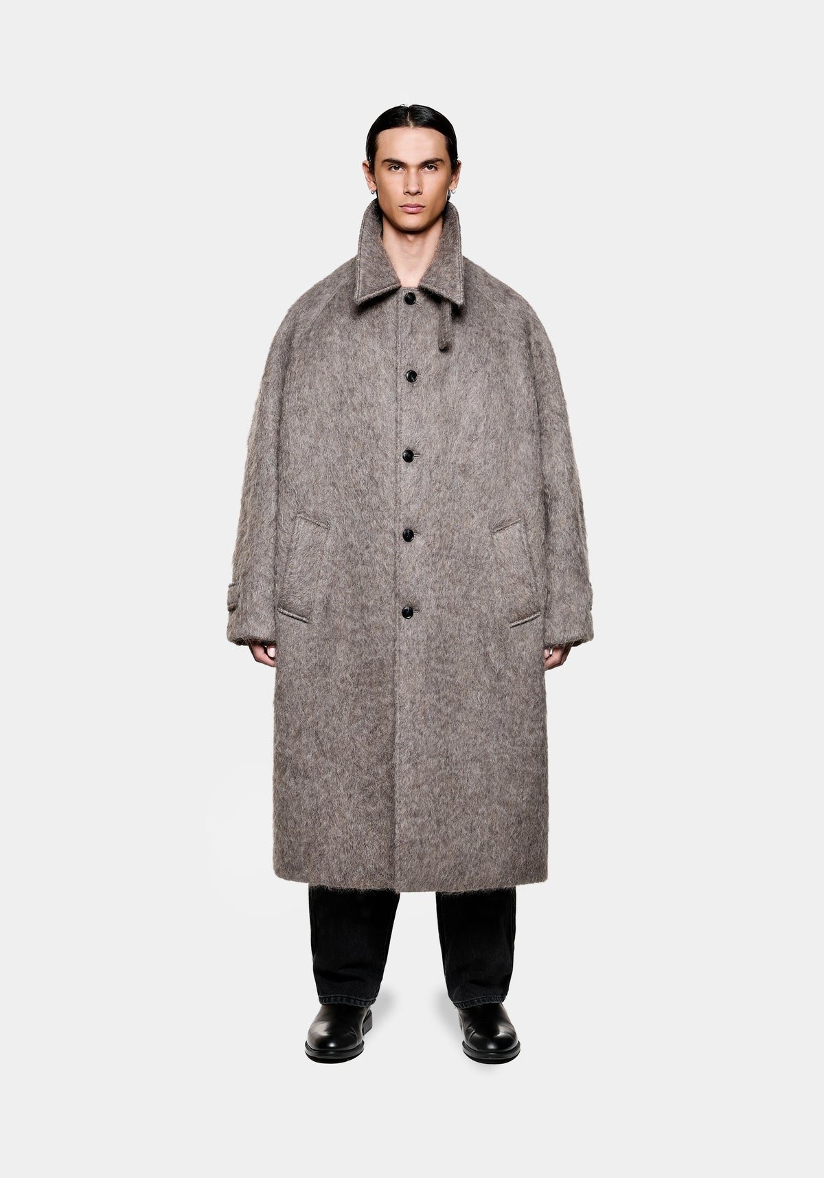 Man wearing a long grey textured wool coat with black buttons over black trousers and black leather shoes
