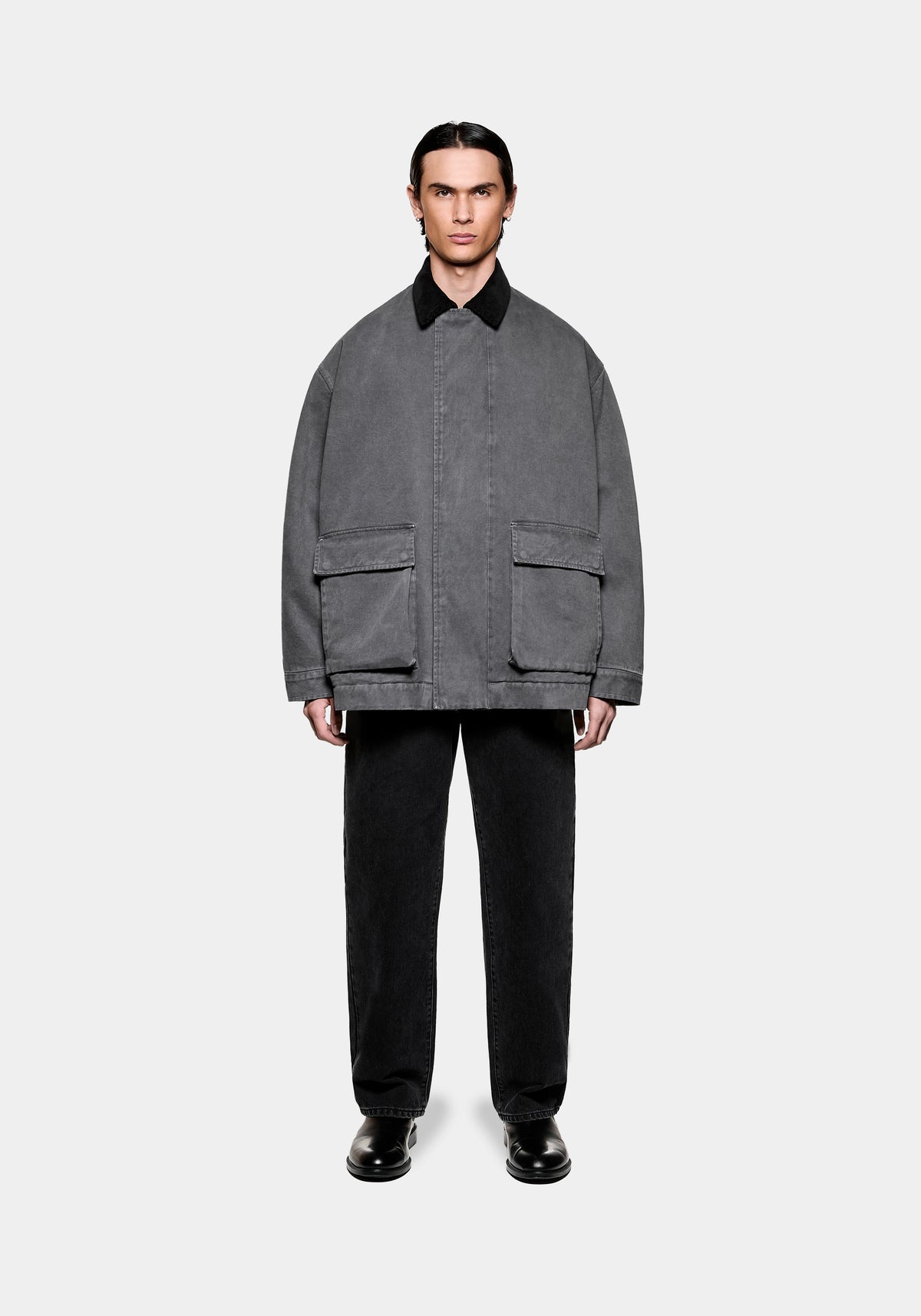Man wearing a grey oversized jacket with a black collar and large front pockets paired with black trousers