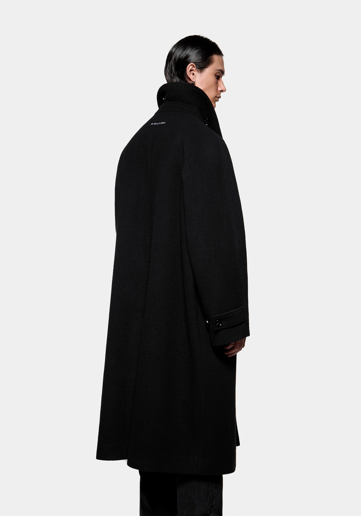 Person wearing a long black wool coat viewed from the side