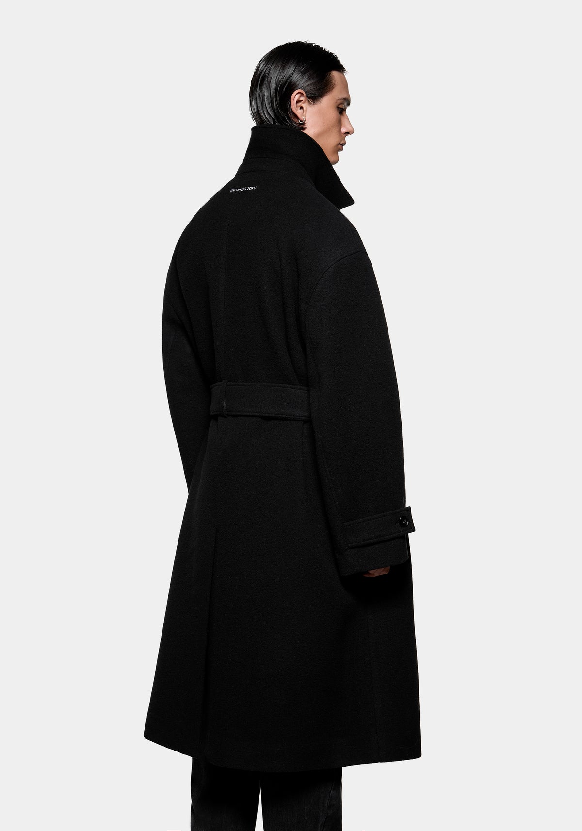 Person wearing a black belted wool coat viewed from the back