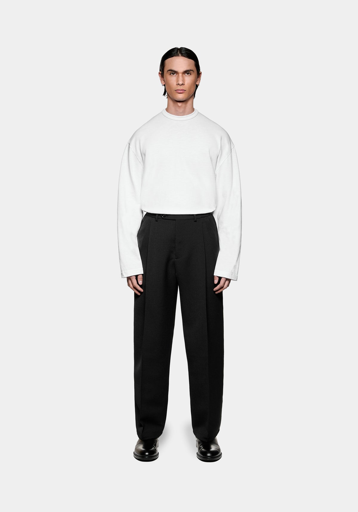 Model wearing a white long sleeved t-shirt and black tailored trousers with black leather shoes