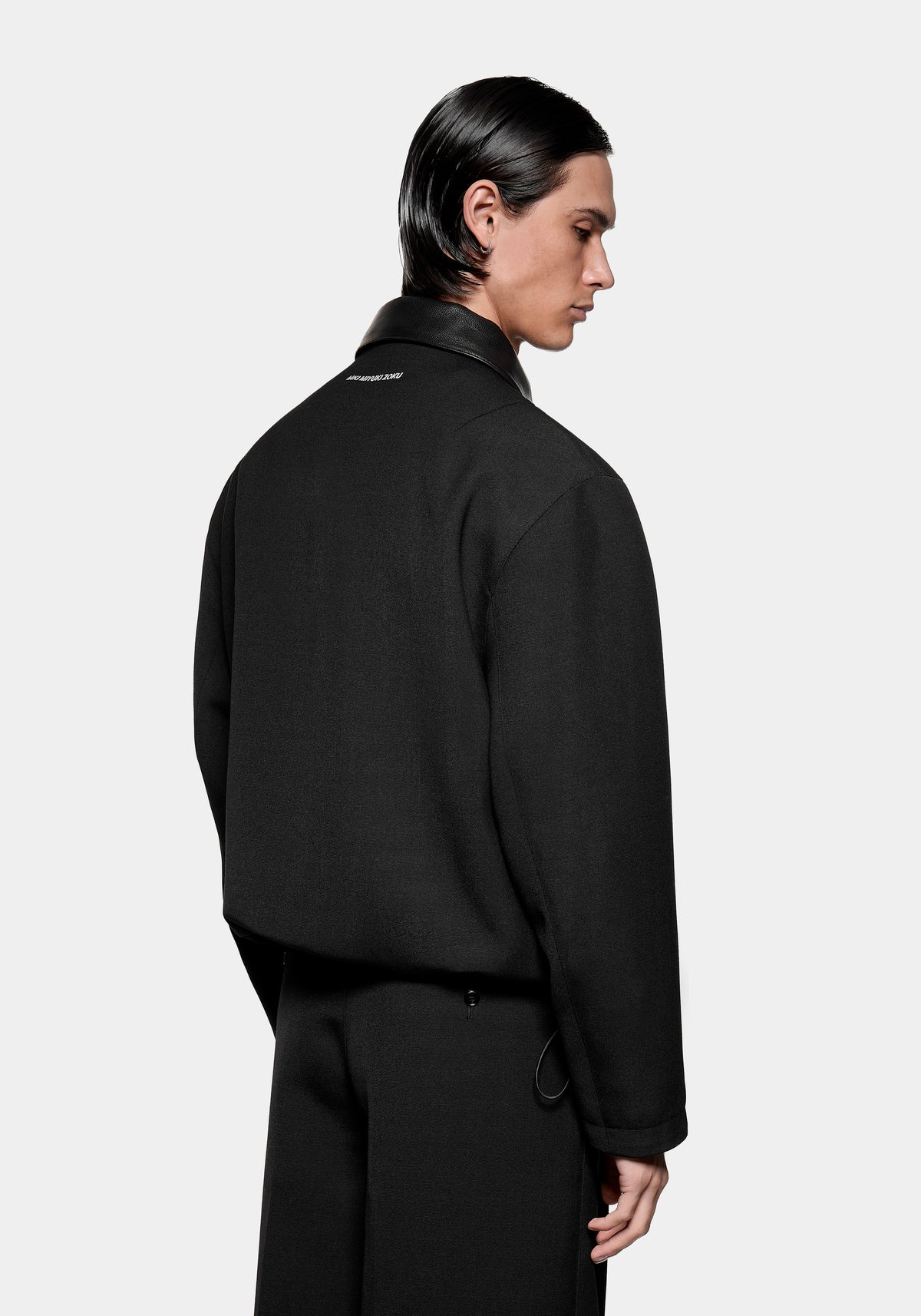Man wearing a black jacket with a leather collar and white branding on the back