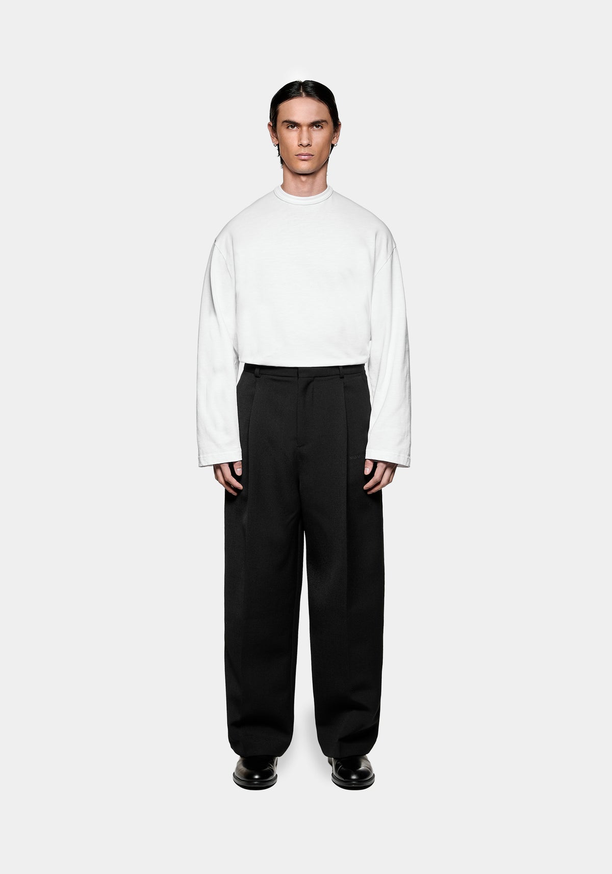 Man wearing a white long sleeved top and black tailored trousers