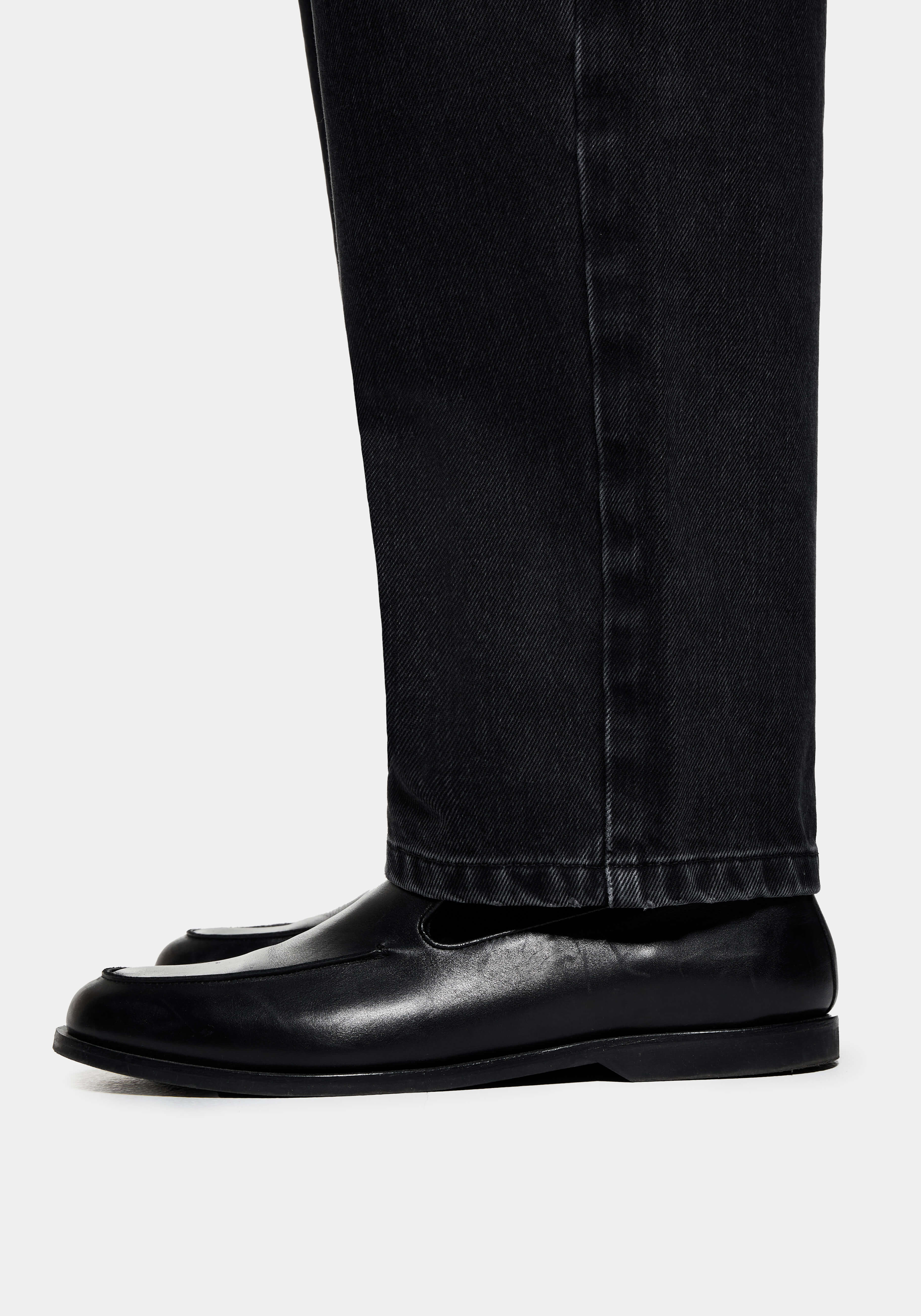 Close-up of the straight hem of the Black Wash jeans falling over black loafers