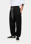 Front three-quarter view of the Black Superweight Joggers showing the heavy drape and cuffed hems over black slip ons