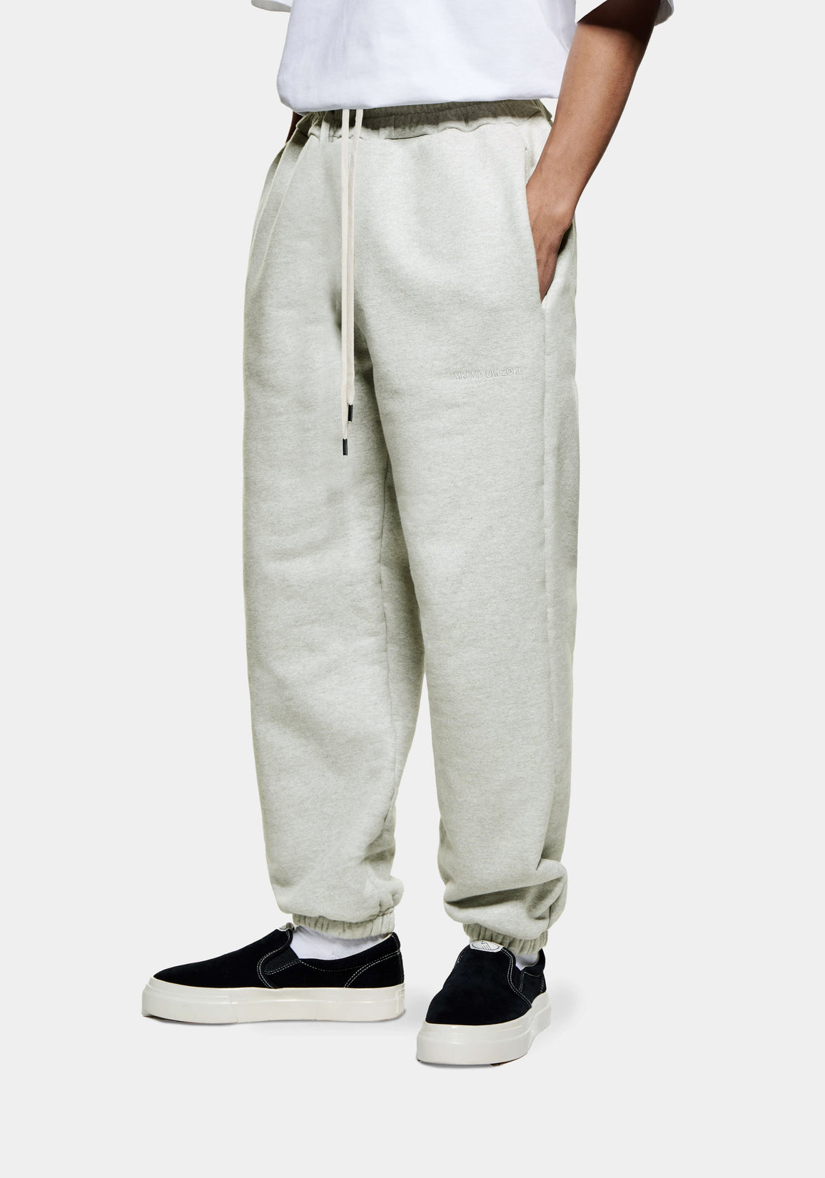Front three-quarter view of the Oatmeal Superweight Joggers showing the heavy drape and cuffed hems over black slip ons
