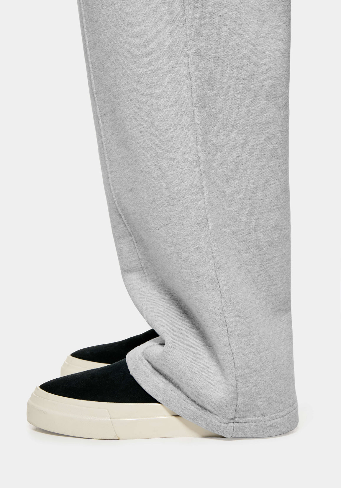 Close-up of the open hem of the Grey joggers falling over black slip ons