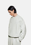 Three-quarter view of the oversized oatmeal Superweight crewneck showing the heavy drape and dropped shoulders