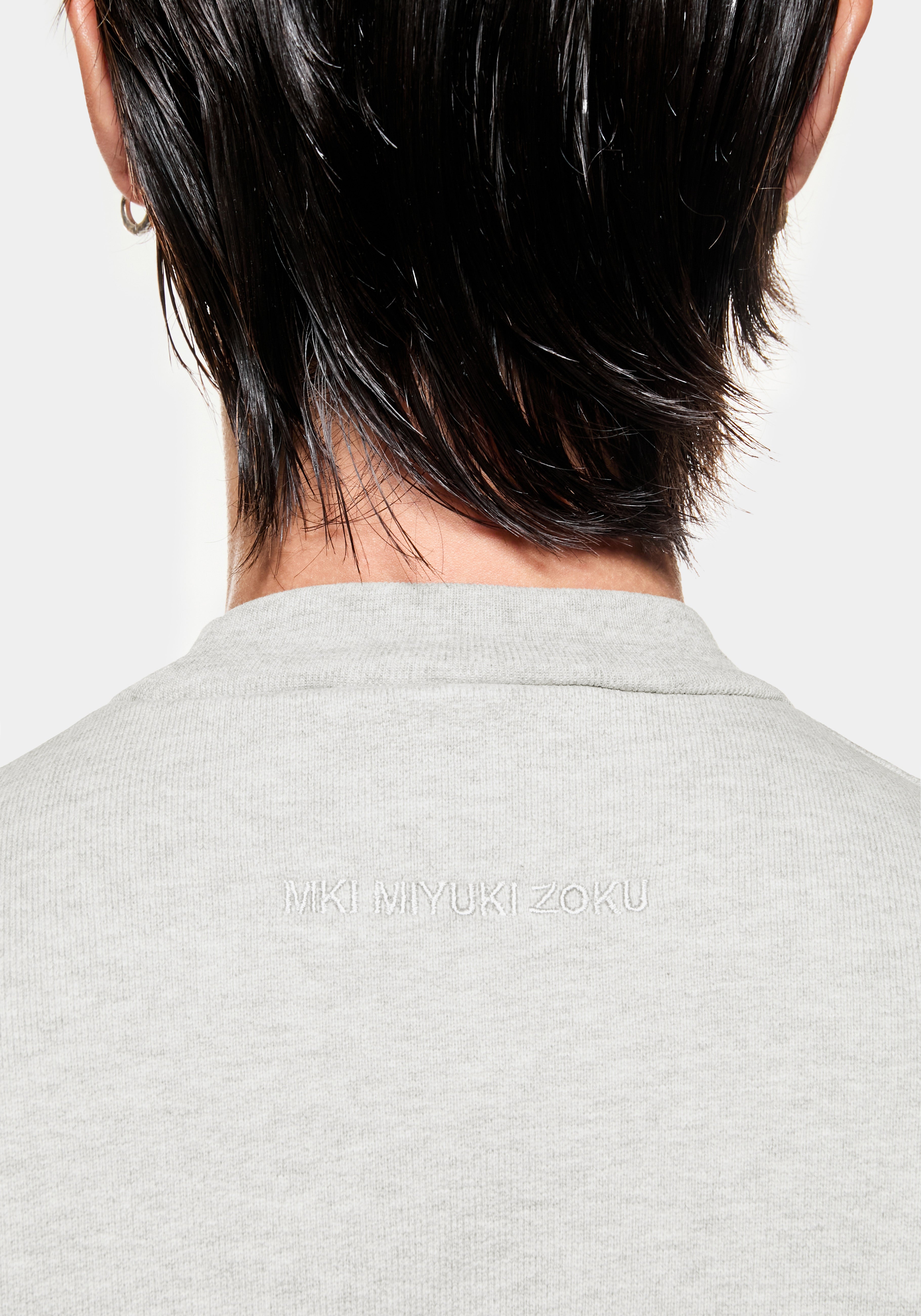 Close-up of the tonal MKI MIYUKI ZOKU logo embroidered below the back neck of the oatmeal crewneck