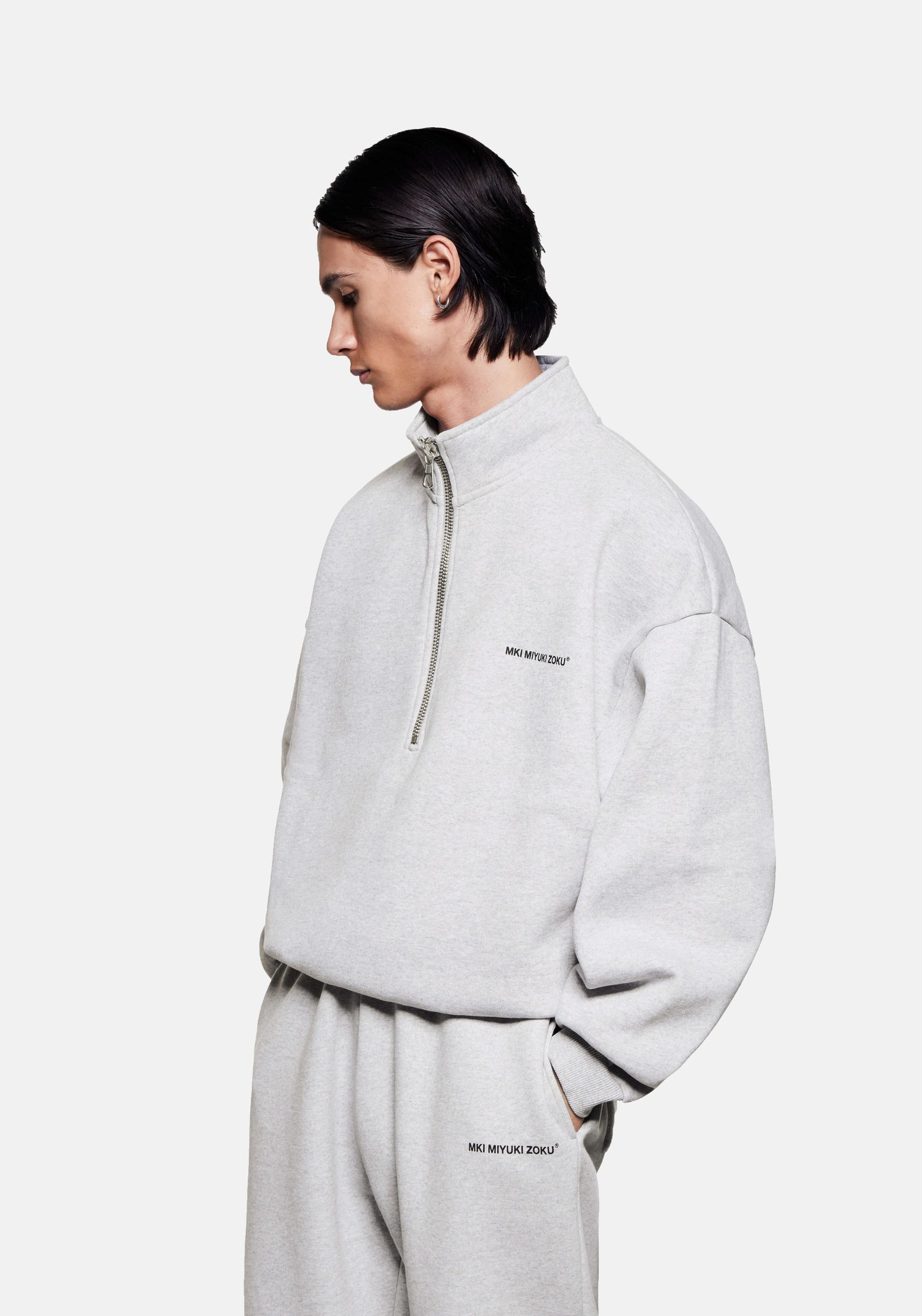 Front side view of the MKI Uniform Jersey Quarter Zip Pullover Top in grey with black printed branding in a boxy oversized fit